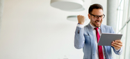 Hombre con gafas, tiene una tableta en la mano, al mirar la tableta genera gesto de celebración